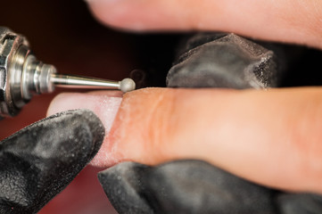 The master of nail extensions makes a hardware manicure and covers the nails with gel varnish in the beauty salon