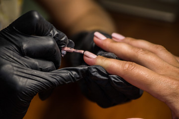 The master of nail extensions makes a hardware manicure and covers the nails with gel varnish in the beauty salon