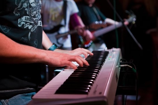 Musician's hands playing synthesizer at a live show in a pub with other men playing guitars