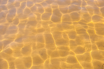 Transparent sea water with sunny glares and sandy bottom. Top view.