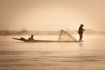 A fisherman with his child goes fishing on a boat with a typical fish net early morning during a sunrise on the Inle Lake, Myanmar (Burma)