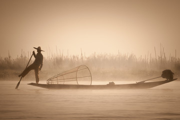 A fisherman goes fishing on a boat with a typical fish net early morning during a sunrise on the Inle Lake, Myanmar (Burma)