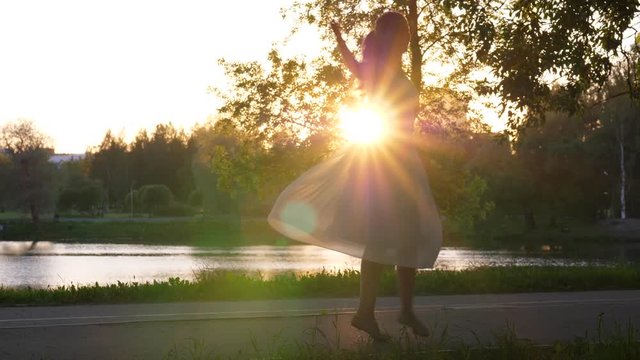 Girl spin around in airy dress against setting sun.