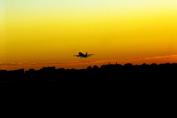 Fototapeta na wymiar airplane take off at sunset yellow sun silhouettes of buildings