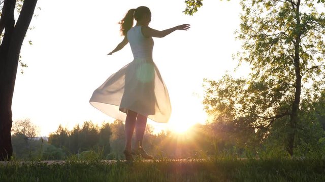 Young woman dancing and spinning around against evening sun