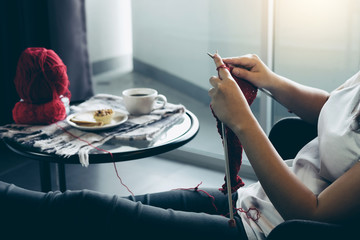 Close up shot of young woman hands knitting a red scarf handicraft in the living room on terrace at home