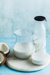 natural, homemade coconut milk in a glass jar, jar and glass. and halves of chopped natural coconut. on a marble board. on the blue
