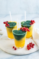 two colored fresh smoothies in glasses with fresh berries. orange banana juice with spirulina powder. detox breakfast. healthy eating