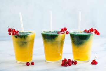 two colored fresh smoothies in glasses with fresh berries. orange banana juice with spirulina powder. detox breakfast. healthy eating
