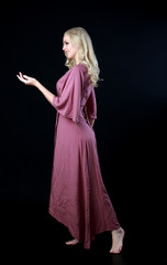 full length portrait of blonde girl wearing long purple dress. standing pose. black studio background.