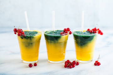 two colored fresh smoothies in glasses with fresh berries. orange banana juice with spirulina powder. detox breakfast. healthy eating