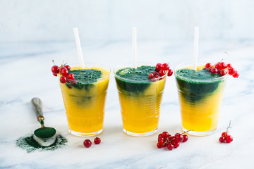 two colored fresh smoothies in glasses with fresh berries. orange banana juice with spirulina powder. detox breakfast. healthy eating
