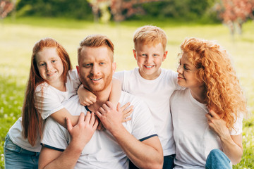 beautiful happy redhead family hugging and smiling at camera in park