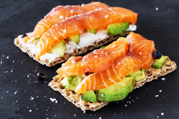 Two healthy protein crisp sandwiches with avocado and smoked salmon. Slate background. Selective focus.