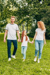 happy family with one child holding hands and walking together in park