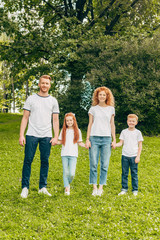 Obraz premium happy family with two kids holding hands and smiling at camera in park