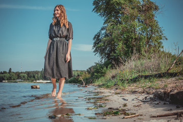 a woman walks along the river's edge and looking away