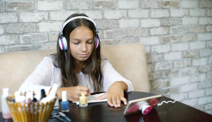 Fototapeta na wymiar Cute teenager girl in headphones listening music on phone while making manicure applying nail polish with free copy space. Beauty, bodycare, wellness, hygiene, communication, leisure time concept.
