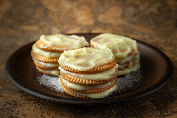 Obraz na płótnie Canvas Cookies smeared with custard cream on a dark plate against a dark background