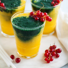 two colored fresh smoothies in glasses with fresh berries. orange banana juice with spirulina powder. detox breakfast. healthy eating
