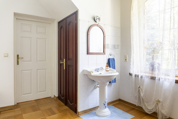 Real photo of a classic bedroom interior with doors, wash basin, mirror and window decorated with curtains