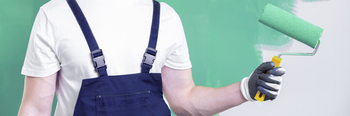 Close-up on a home renovation crew person in workwear holding a roller with a neo mint paint and a...