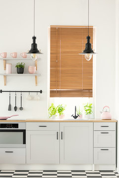 Real photo of a modern kitchen interior with wooden window blinds, cupboards, plants and pink details