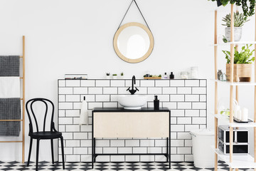 Mirror above washbasin in white bathroom interior with plants and black chair next to ladder. Real photo