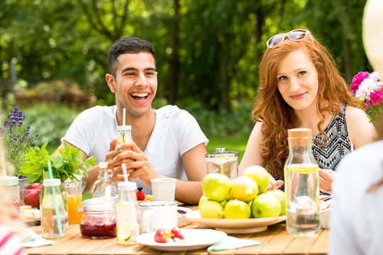 Smiling spanish man and happy woman drinking and eating during party in the garden