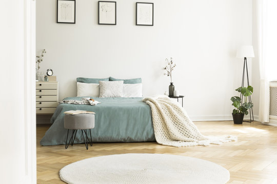 White round rug in front of green bed with blanket in bedroom interior with posters. Real photo