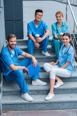 smiling multicultural medical students sitting on stairs and looking at camera