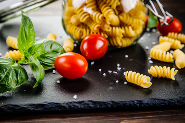 Raw pasta with spices on black stone on wooden background