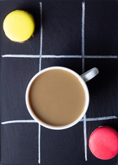 Colourful macarons with a cup of coffee on a dark slate