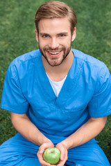 smiling handsome medical student holding apple in hands and looking at camera