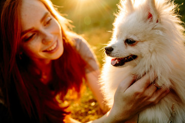 The cute red-haired woman in a hat with a spitz-dog in the park. Beautiful sunset light. Background toning for instagram filter.