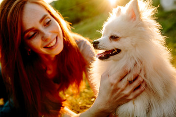 The cute red-haired woman in a hat with a spitz-dog in the park. Beautiful sunset light. Background toning for instagram filter.