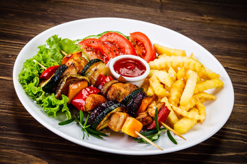 Kebabs - grilled meat with french fries and vegetables on wooden background