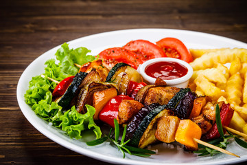 Kebabs - grilled meat with french fries and vegetables on wooden background