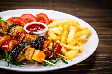Kebabs - grilled meat with french fries and vegetables on wooden background