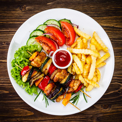 Kebabs - grilled meat with french fries and vegetables on wooden background