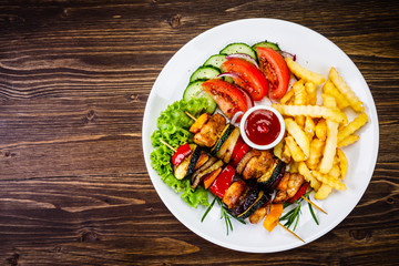 Kebabs - grilled meat with french fries and vegetables on wooden background