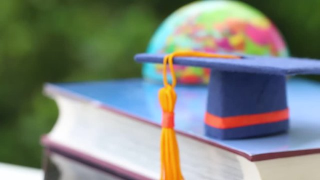 Graduate or Education knowledge learning study abroad concept : Blue Graduation cap on textbook with blur of america earth world globe , blur green light background. Back to School