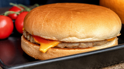 Hamburgers in black tray with small tomato and orange fruit in background