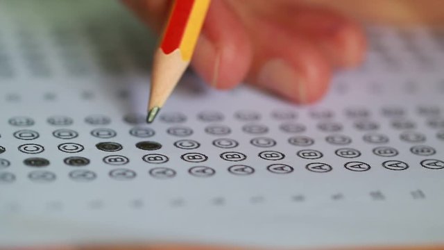 Student taking exams, writing examination on paper answer sheet optical form of standardized test on desk doing final exam in classroom, Examination sitting on row chair in school.

