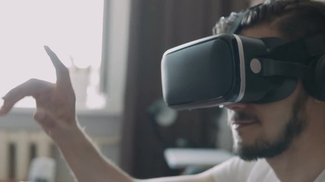 Close up shot of a young bearded man wearing virtual reality glasses - surfing net via virtual reality interface.
