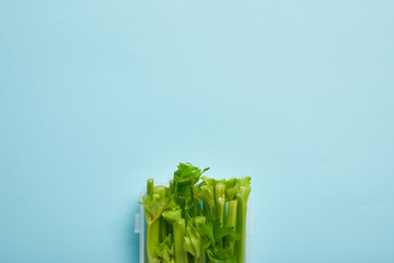 top view of food container full of healthy celery isolated on blue