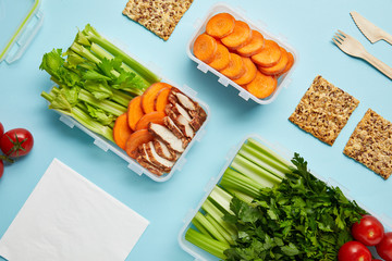 top view of arrangement of food containers with fresh healthy food, napkin and cutlery isolated on blue