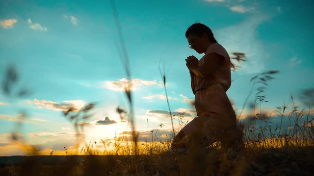 Girl folded her hands in prayer silhouette at sunset. slow motion video. Girl folded her hands in prayer pray to God. girl praying asks forgiveness for sins of repentance. believing girl. concept