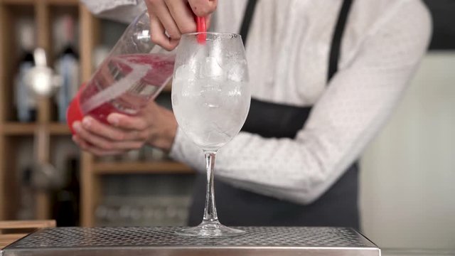A handsome young bartender pours a sparkling water from the soda siphon to the glass with ice cubes. Bar counter. Closeup.