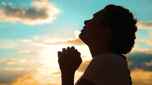 girl praying. girl folded her hands in prayer silhouette at sunset. slow motion video. Girl folded lifestyle her hands in prayer pray to God. asks forgiveness for sins of repentance. believing girl